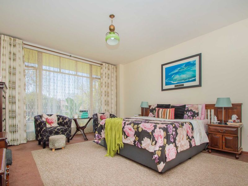 A spacious bedroom featuring large windows that provide ample natural light, neutral wall finishes, and carpeted flooring.