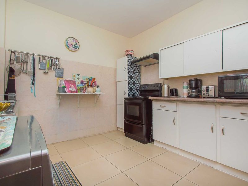 A functional kitchen featuring tiled flooring, a tiled backsplash, built-in cabinetry, and an extractor fan, offering a practical layout for daily cooking needs.