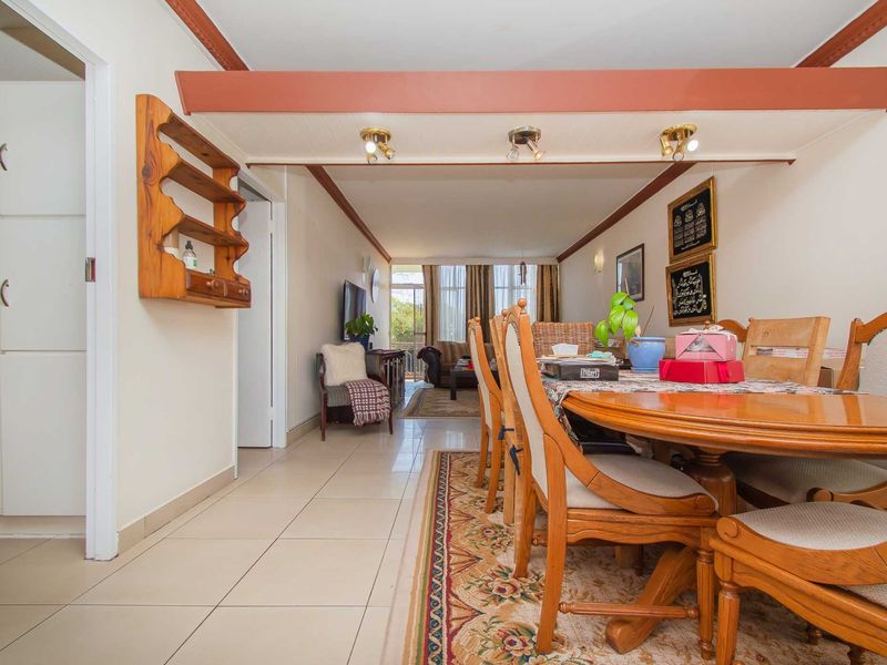 Open-plan living and dining area featuring tiled flooring, a prominent ceiling beam with integrated lighting, and built-in storage cupboards.