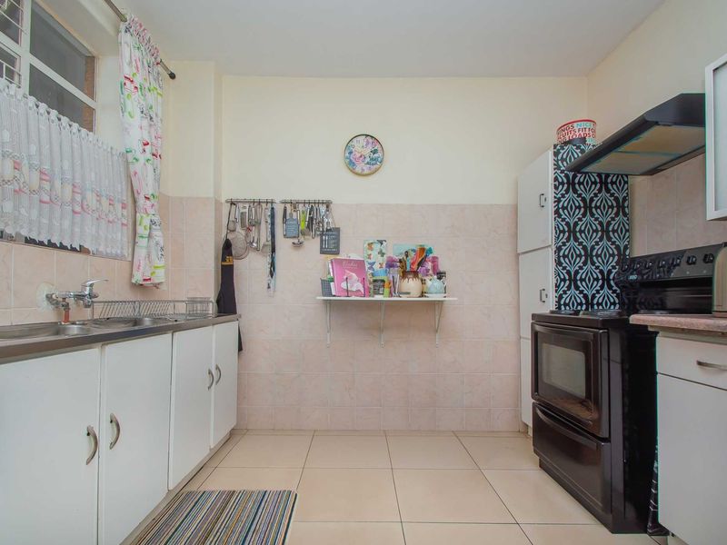 A functional kitchen featuring tiled splashbacks, double basin sink, built-in cabinetry, and an extractor fan, offering a practical layout for daily cooking needs.