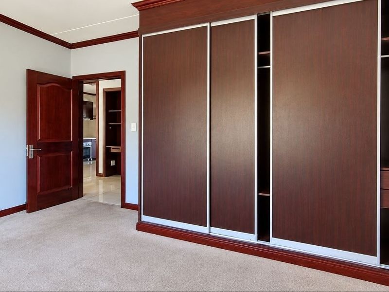 A spacious bedroom featuring neutral carpeting, crown molding, and a large built-in sliding door wardrobe with dark wood finish.