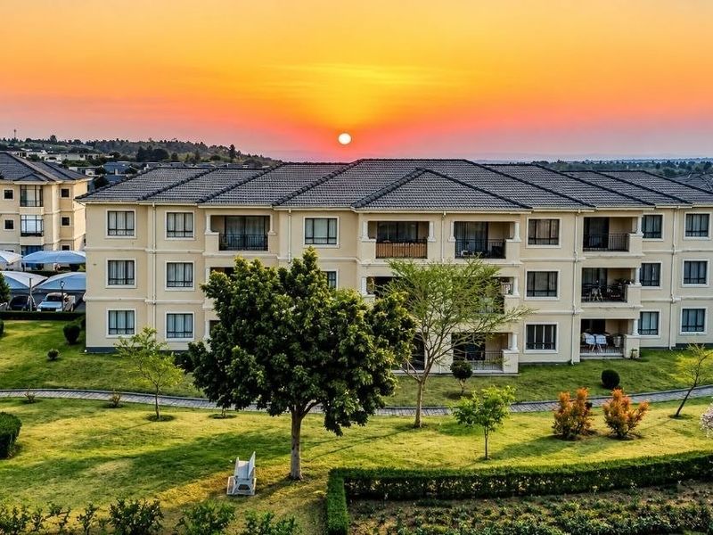Aerial view of a well-maintained apartment complex featuring landscaped gardens, paved walkways, and covered parking areas at sunset.