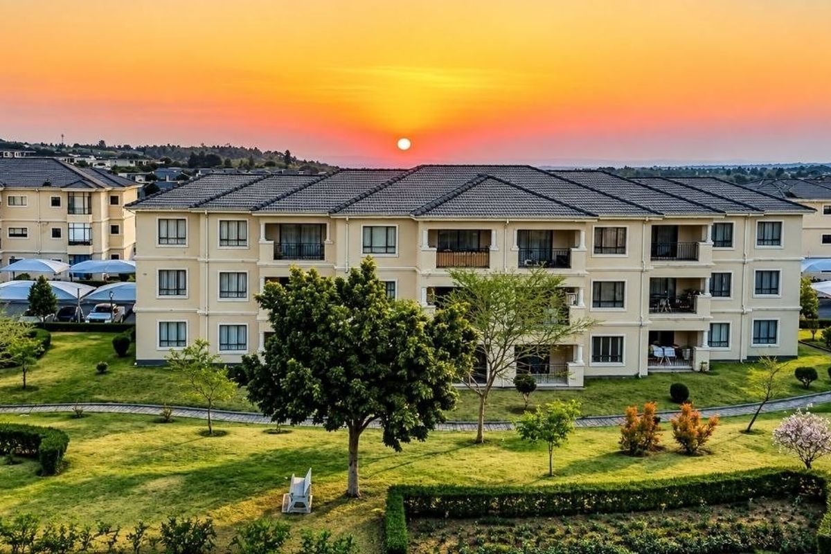 Aerial view of a well-maintained apartment complex featuring landscaped gardens, paved walkways, and covered parking areas at sunset.