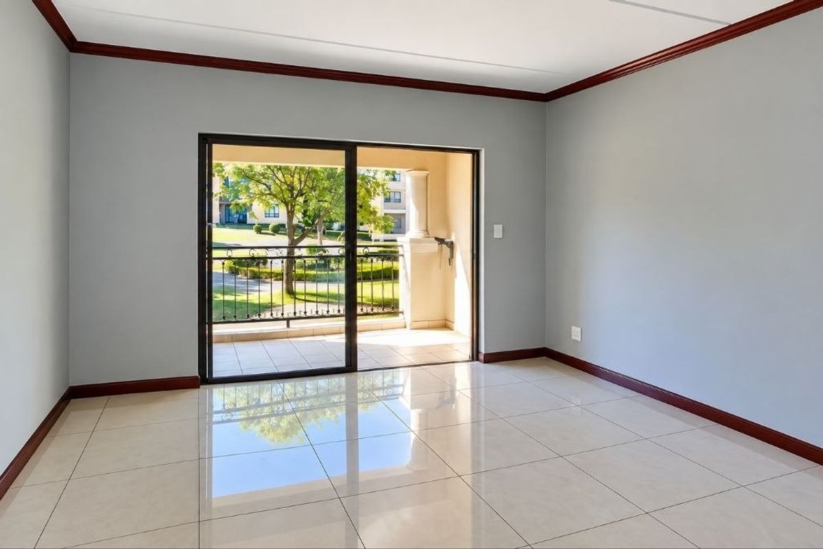A bright, empty living room featuring polished tile flooring, dark wood crown molding, and a sliding glass door leading to a private balcony.