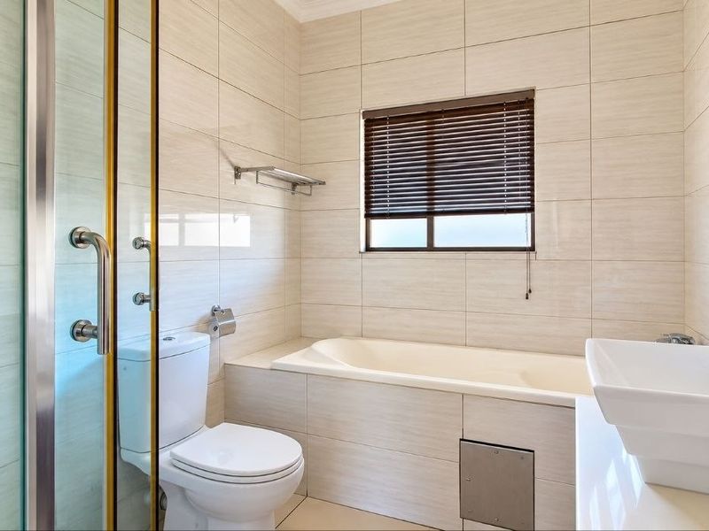 A clean, modern bathroom featuring a built-in bathtub, separate shower enclosure, vanity basin, and neutral wall tiling.