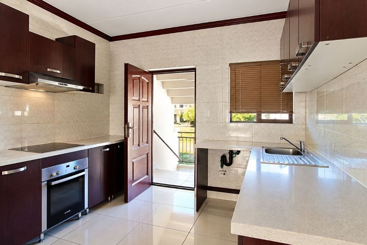 A clean, functional kitchen featuring dark wood cabinetry, stone countertops, built-in oven and hob, and direct access to an exterior staircase.