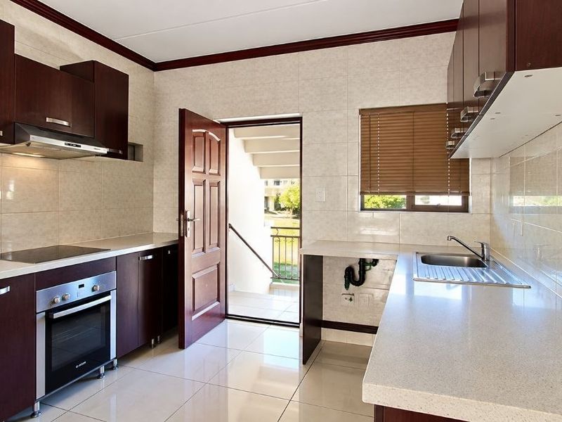 A clean, functional kitchen featuring dark wood cabinetry, stone countertops, built-in oven and hob, and direct access to an exterior staircase.