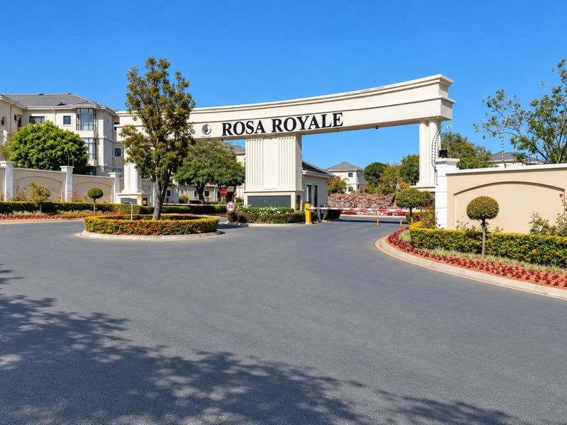 The main entrance to the Rosa Royale apartment complex, featuring a prominent security gatehouse, boom gate access, and well-maintained landscaped surroundings.