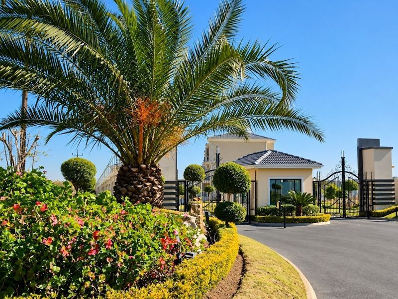 A well-maintained gated entrance to the apartment complex featuring a guard house, manicured landscaping, and a paved driveway.