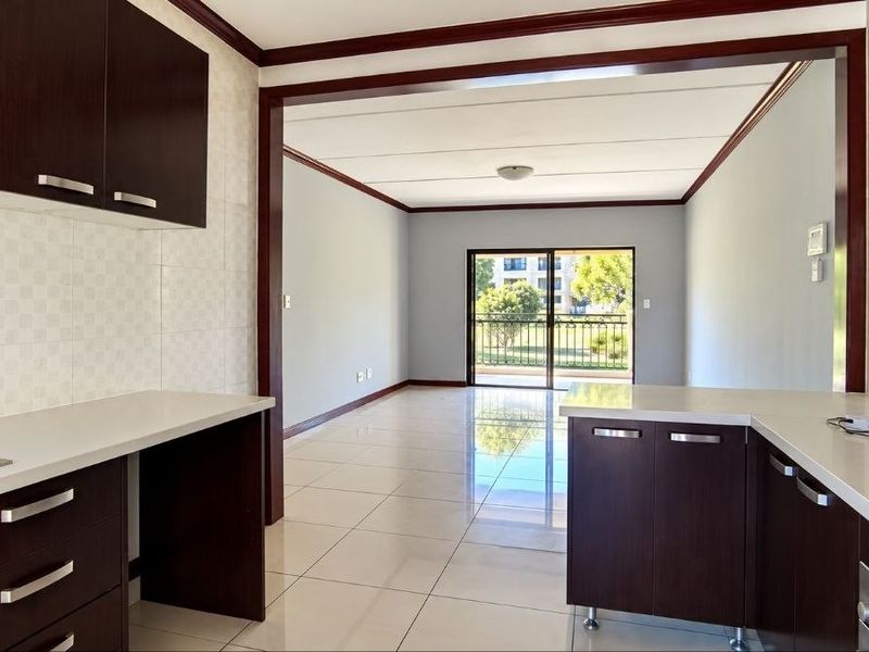 An open-plan kitchen and living area featuring dark wood cabinetry, stone countertops, built-in appliances, and tiled flooring leading to a balcony.
