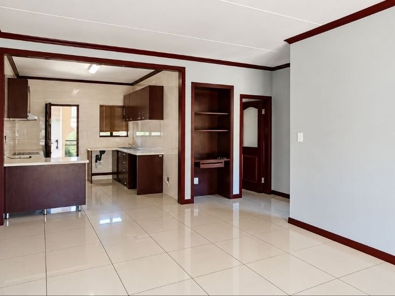 An open-plan living and kitchen area featuring neutral tiled floors, dark wood cabinetry, and built-in shelving, offering a clean and functional layout.