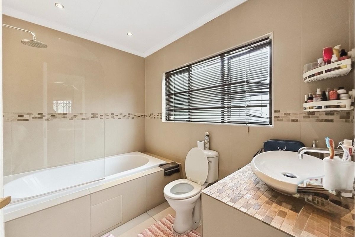 A functional bathroom featuring a built-in bathtub with an overhead shower, a vessel sink on a tiled vanity, and a toilet.