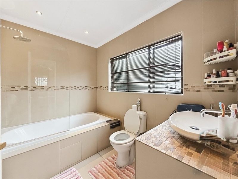 A functional bathroom featuring a built-in bathtub with an overhead shower, a vessel sink on a tiled vanity, and a toilet.