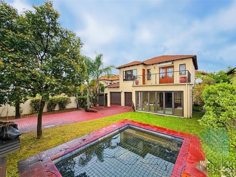 Rear view of a two-story house featuring a swimming pool with safety net, paved driveway, double garage, and an upper-level balcony.
