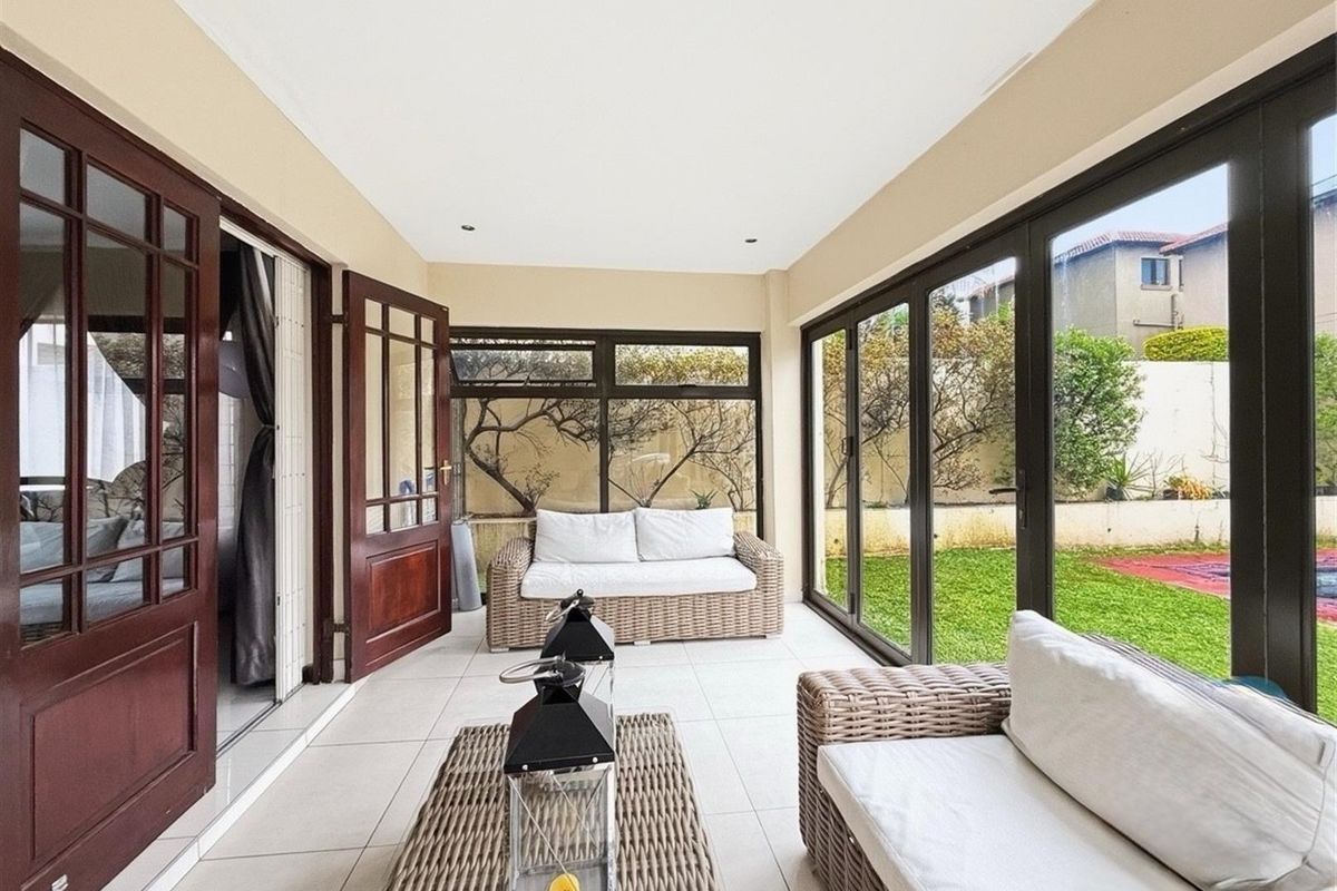 A bright, enclosed patio featuring tiled flooring, recessed lighting, and extensive glass doors providing seamless access to the garden and pool area.