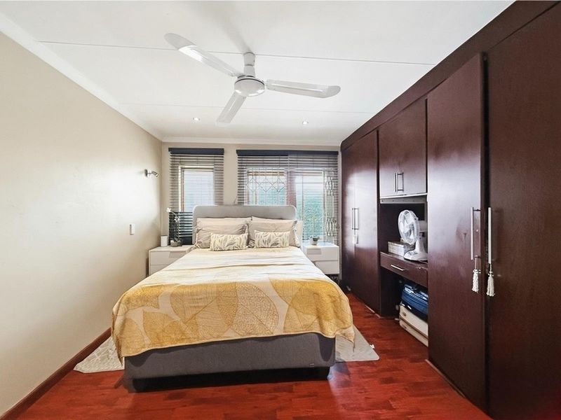A well-maintained bedroom featuring dark wood built-in cupboards, laminate flooring, a ceiling fan, and venetian blinds.