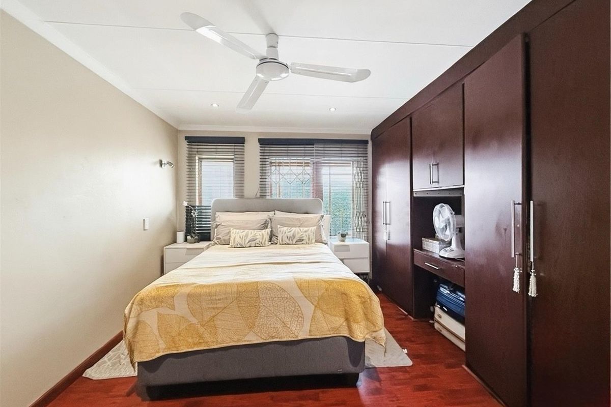 A well-maintained bedroom featuring dark wood built-in cupboards, laminate flooring, a ceiling fan, and venetian blinds.