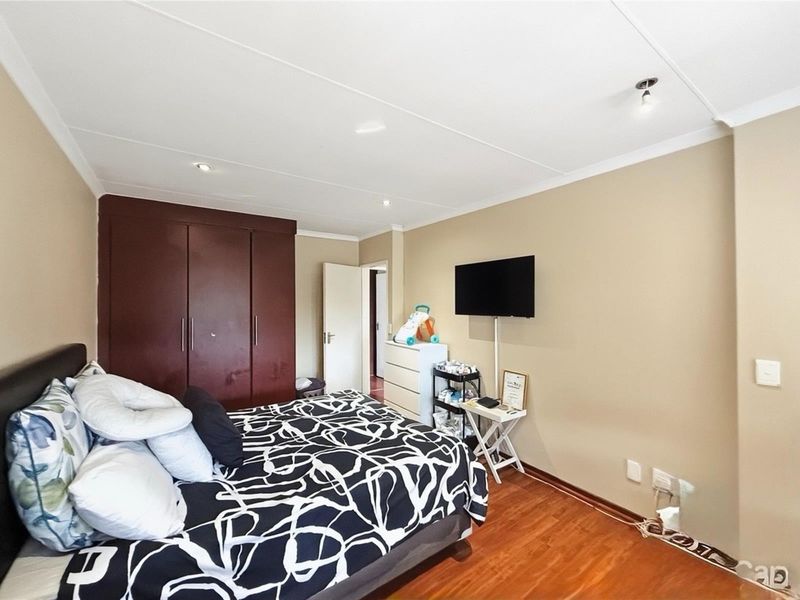 A bedroom featuring laminate flooring, recessed downlighting, and dark-toned built-in cupboards.