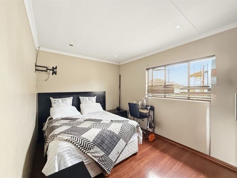 A well-maintained bedroom featuring laminate flooring, recessed downlighting, and venetian blinds, providing a clean and functional living space.