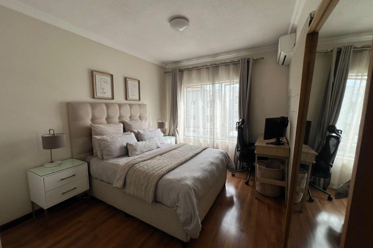 A well-maintained bedroom featuring laminate flooring, an integrated air conditioning unit, and a large built-in wardrobe with mirrored doors.