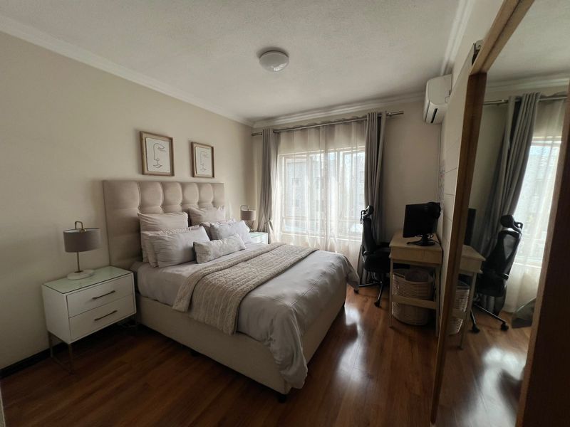 A well-maintained bedroom featuring laminate flooring, an integrated air conditioning unit, and a large built-in wardrobe with mirrored doors.