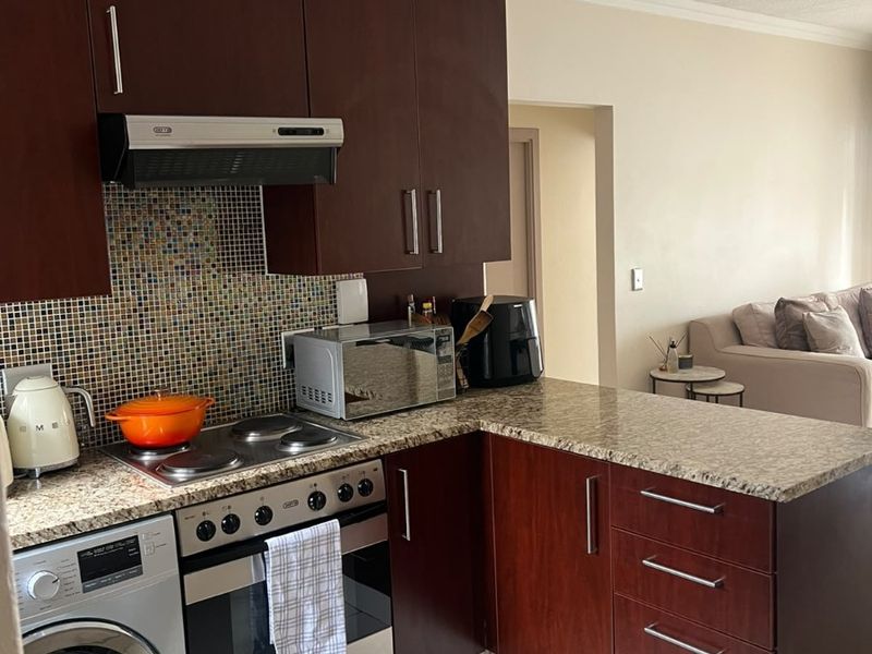 Compact kitchen featuring dark wood cabinetry, granite countertops, mosaic tile backsplash, and integrated appliances including an oven, hob, and washing machine.