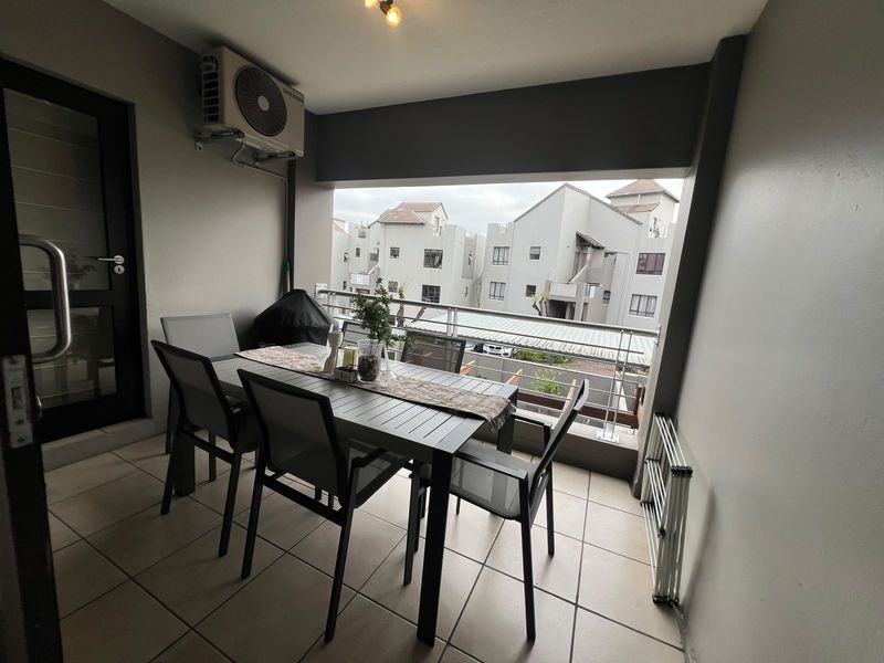 A covered balcony featuring tiled flooring, a mounted air conditioning unit, and metal safety railings, offering an outdoor space for relaxation.