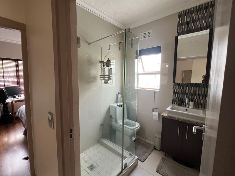A functional bathroom featuring a glass shower enclosure, modern vanity cabinet with basin, and decorative tiled wall accents.