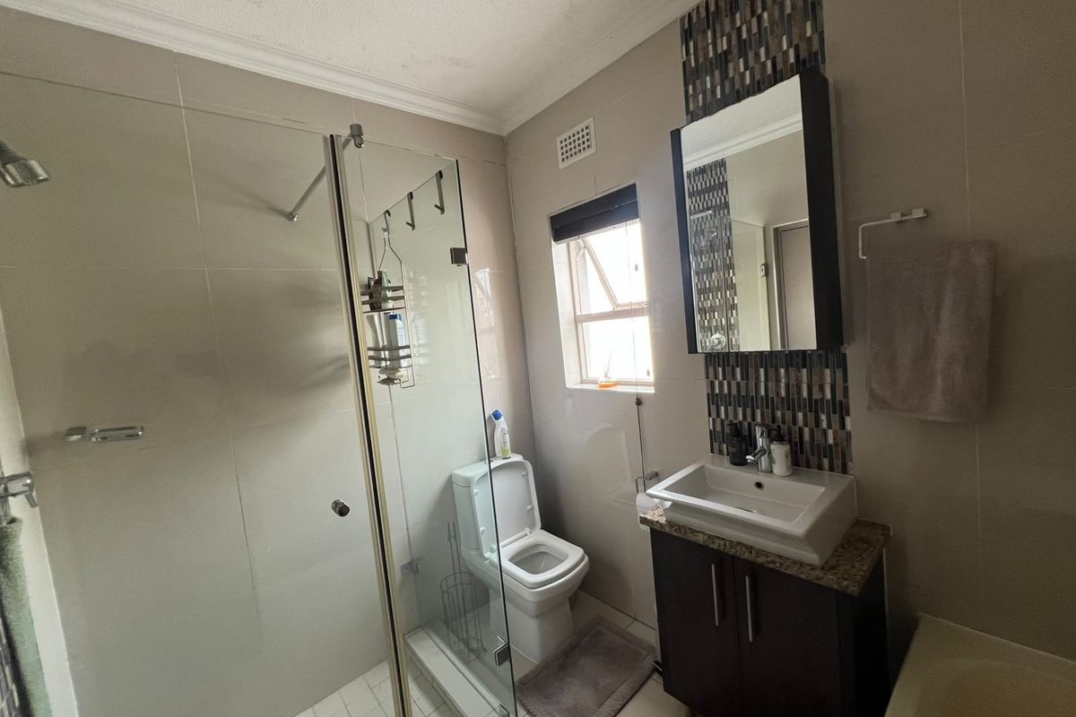 A well-maintained bathroom featuring a glass shower enclosure, a modern vanity with basin, and a decorative mosaic tile accent wall.