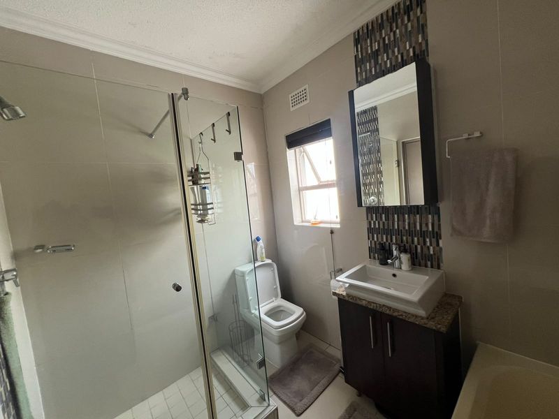 A well-maintained bathroom featuring a glass shower enclosure, a modern vanity with basin, and a decorative mosaic tile accent wall.