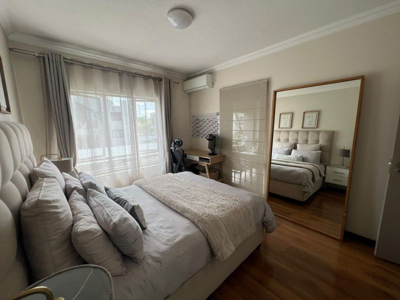 A well-maintained bedroom featuring hardwood flooring, an integrated air conditioning unit, and large windows with curtain tracks, offering a comfortable and functional living space.