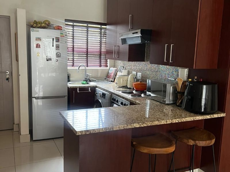 Compact kitchen featuring dark wood cabinetry, granite countertops, a mosaic tile backsplash, and a convenient breakfast bar for casual dining.