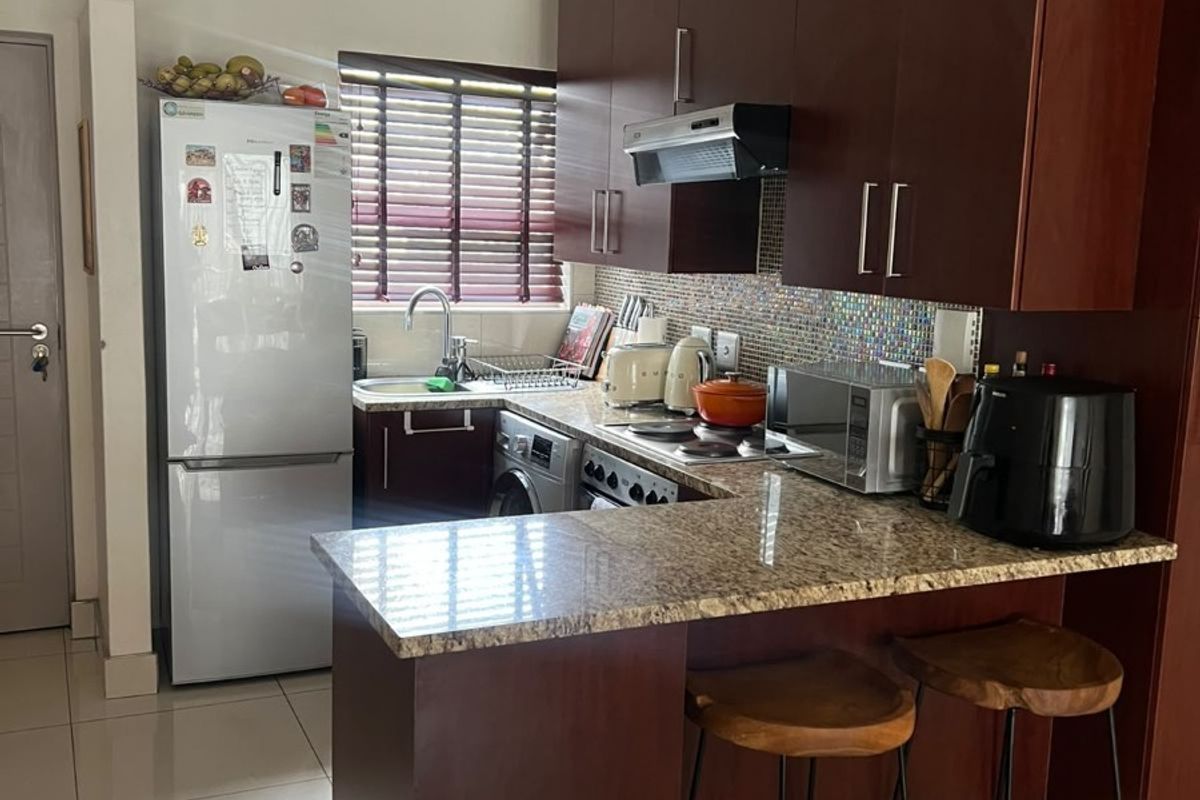 Compact kitchen featuring dark wood cabinetry, granite countertops, a mosaic tile backsplash, and a convenient breakfast bar for casual dining.