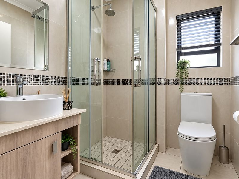 Modern bathroom featuring a glass shower enclosure, vanity with vessel sink, toilet, and neutral wall tiling with a decorative mosaic border.