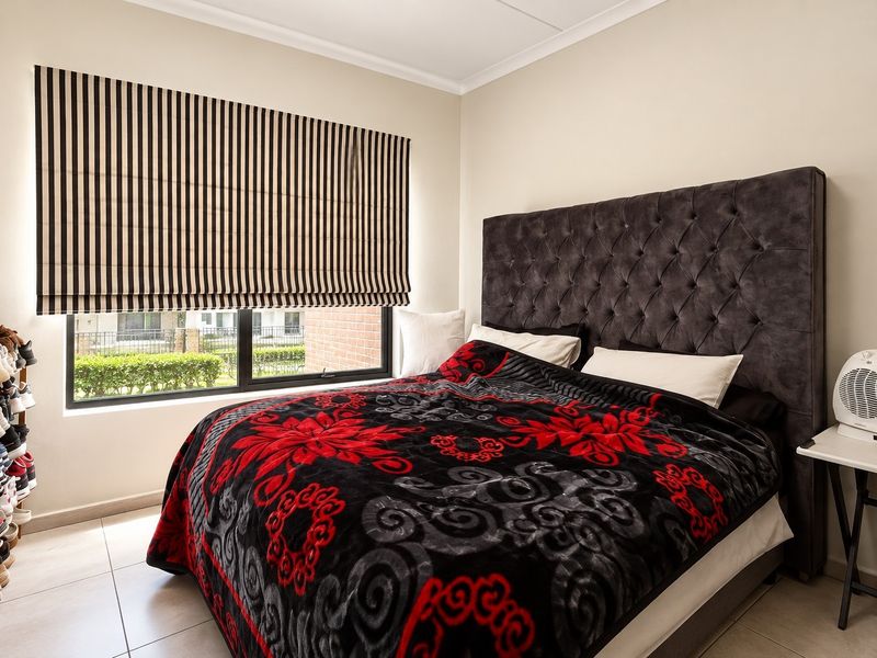 A well-maintained bedroom featuring tiled flooring, a large window with a striped roman blind, and neutral wall finishes.