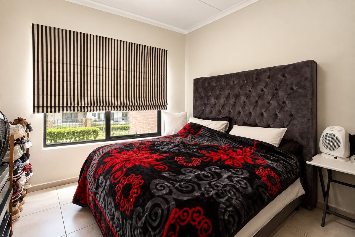 A well-maintained bedroom featuring tiled flooring, a large window with a striped roman blind, and neutral wall finishes.