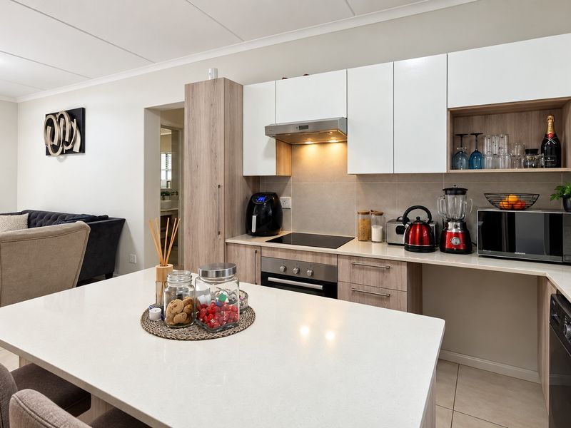 Modern open-plan kitchen featuring sleek white and wood-tone cabinetry, stone countertops, and integrated appliances, seamlessly flowing into the adjacent living area.