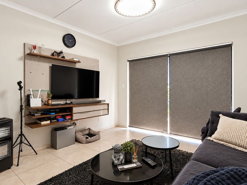 A well-maintained living room featuring tiled flooring, a modern built-in media console, and large windows fitted with roller blinds.