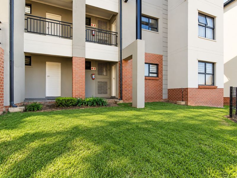 A well-maintained apartment exterior featuring a brick and plaster facade, balcony access, and a neat lawn area.