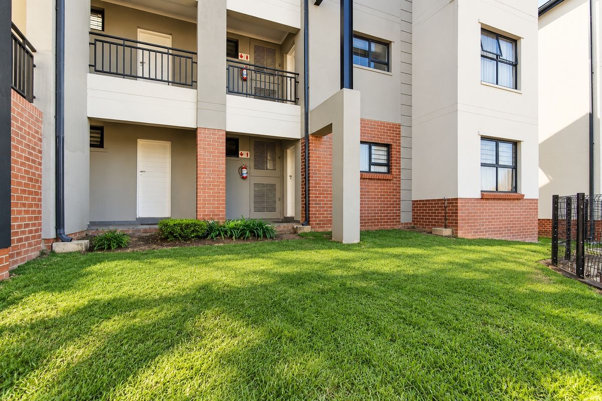 A well-maintained apartment exterior featuring a brick and plaster facade, balcony access, and a neat lawn area.
