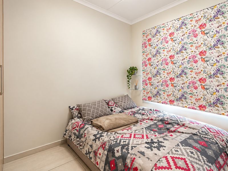 A well-maintained bedroom featuring neutral tiled flooring, a built-in wardrobe, and a decorative floral feature wall.