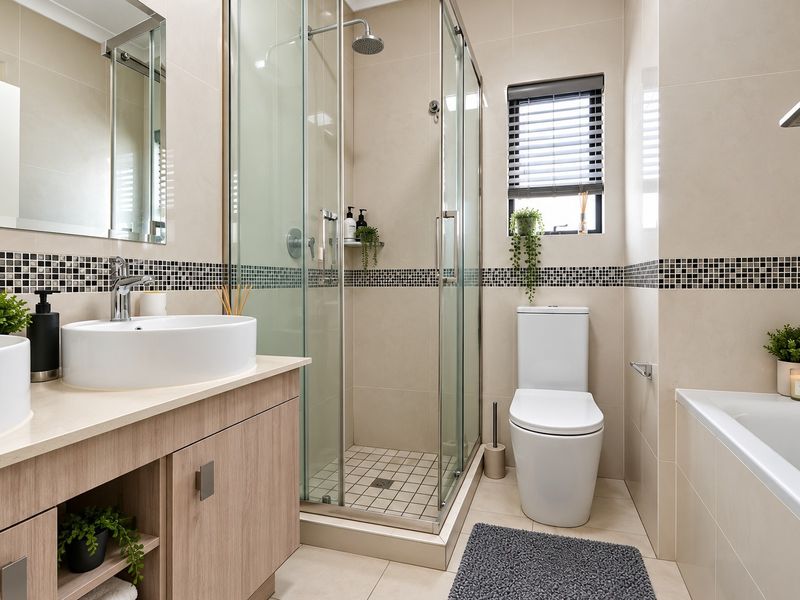 Modern bathroom featuring a dual vanity, glass-enclosed shower, bathtub, and neutral wall tiling with a decorative mosaic border.