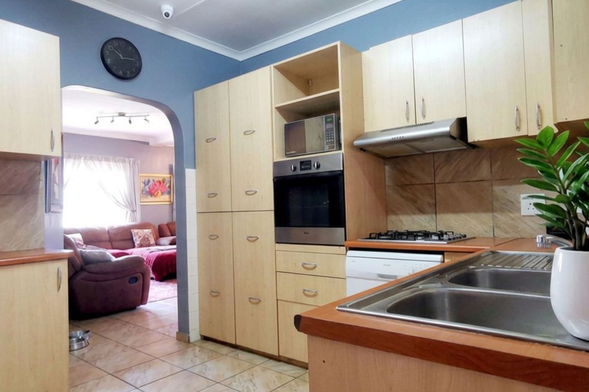 Functional kitchen featuring light wood cabinetry, built-in oven, gas hob, extractor fan, and double bowl sink, with an open archway leading to the living area.