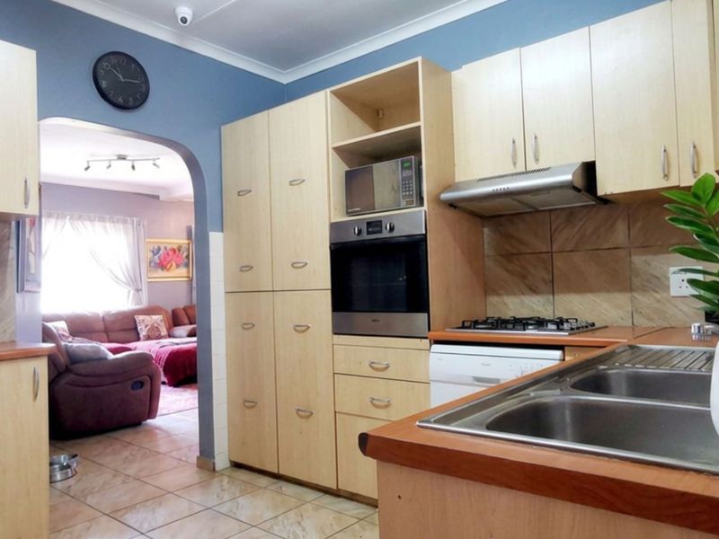 Functional kitchen featuring light wood cabinetry, built-in oven, gas hob, extractor fan, and double bowl sink, with an open archway leading to the living area.