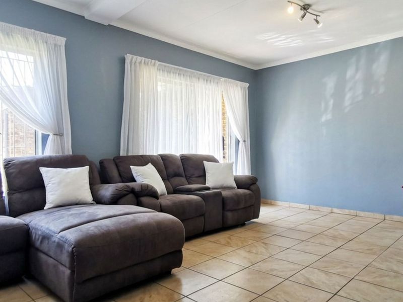 A bright living room featuring neutral tiled flooring, blue painted walls, and built-in wall shelving, offering a clean and functional living space.