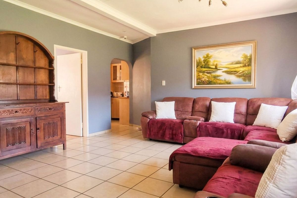 A spacious living room featuring neutral tiled flooring, coved ceilings, and an arched entryway leading to the kitchen area.