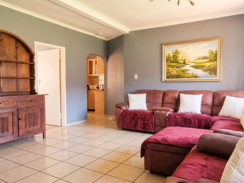 A spacious living room featuring neutral tiled flooring, coved ceilings, and an arched entryway leading to the kitchen area.