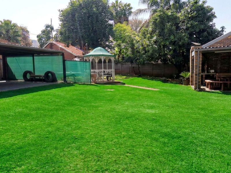Spacious rear garden featuring a well-maintained lawn, a covered carport, a brick-built patio area, and a decorative gazebo.