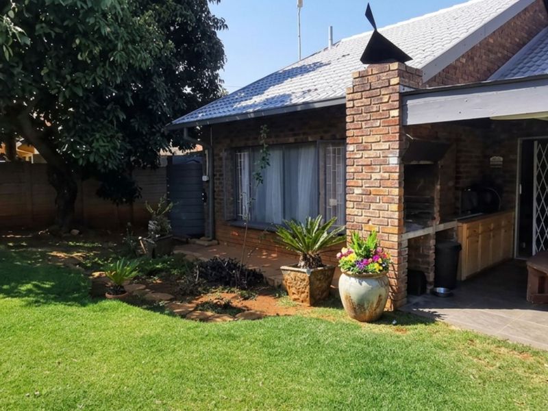 Rear exterior view featuring a brick-built fireplace, covered patio area, and a well-maintained garden with a boundary wall.