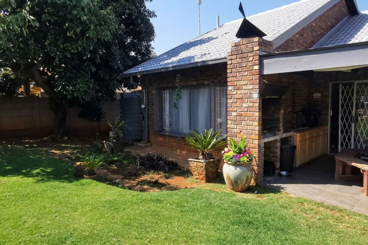 Rear exterior view featuring a brick-built fireplace, covered patio area, and a well-maintained garden with a boundary wall.